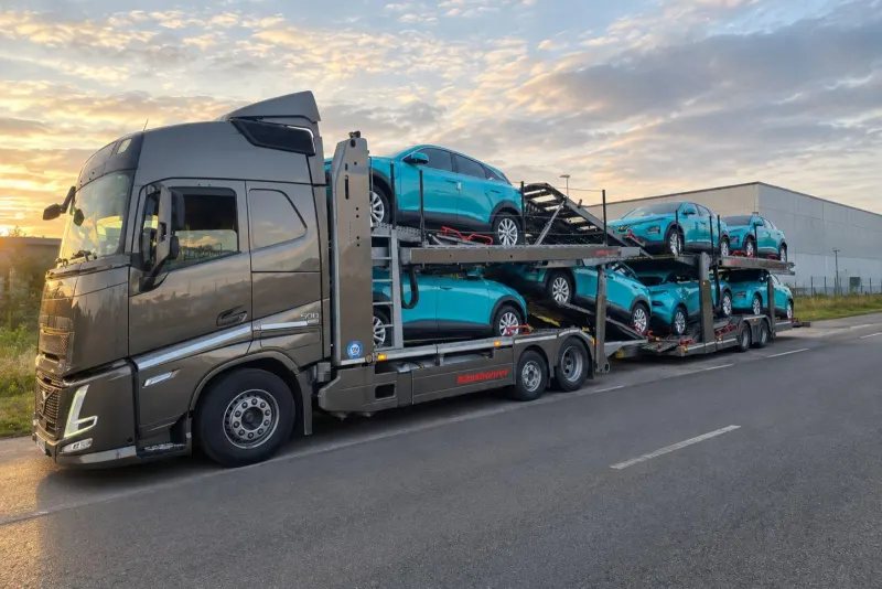 „Volvo“ autovežis su turkio spalvos automobiliais saulėtekio metu